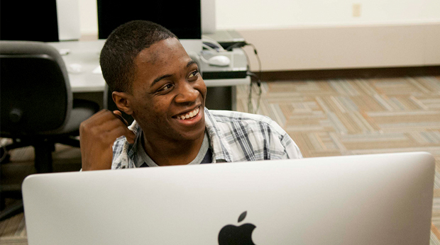 A student smiles from behind his computer in a lab at La Roche University.